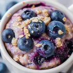 Blueberry mug muffin topped with fresh blueberries and oats in a white mug